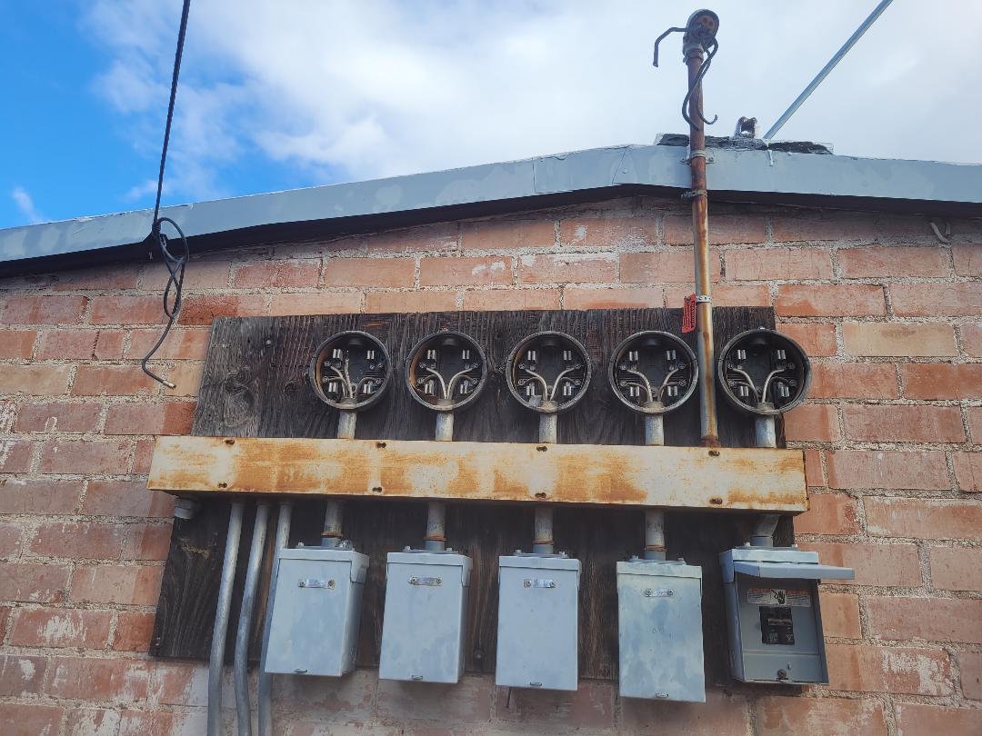 Existing aged dual-meter service on brick wall before replacement